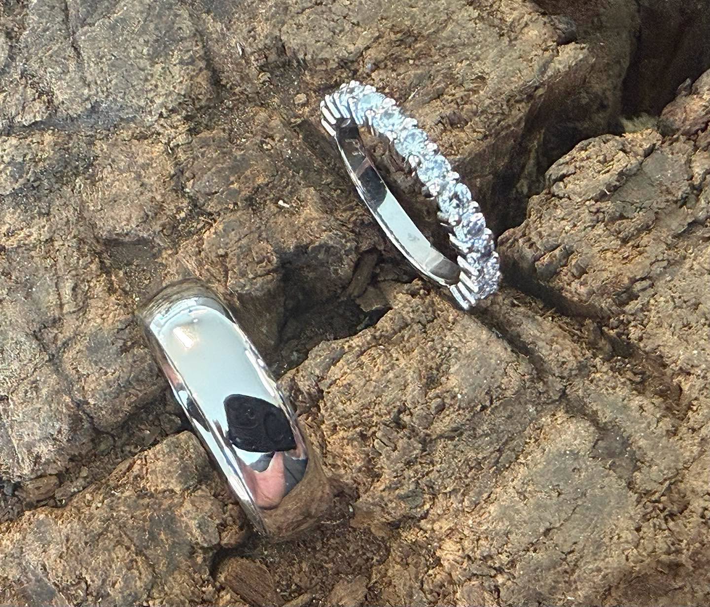A plain white-metal band and a stone-set band on bark