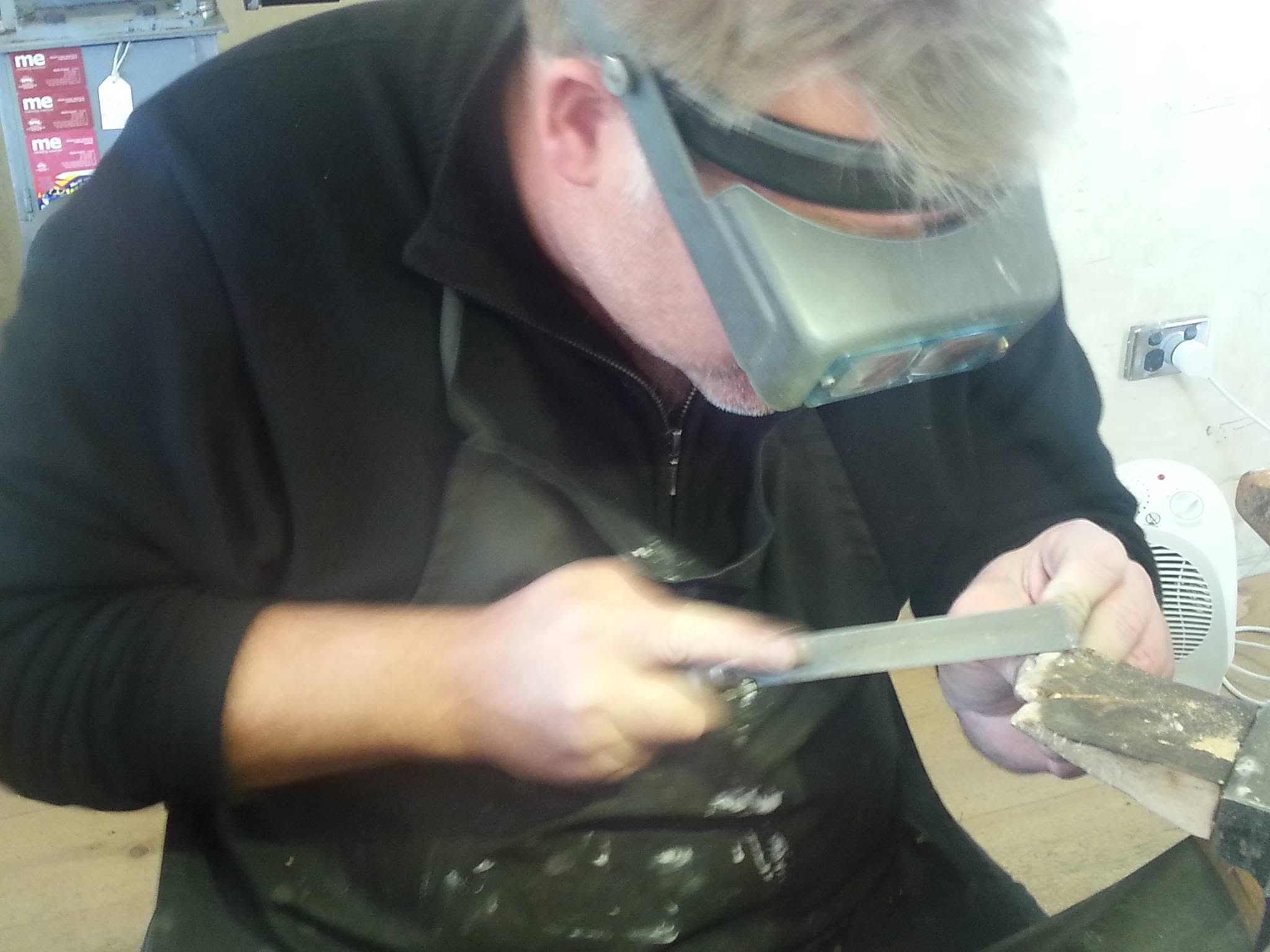 A jeweller wearing a magnifying visor, working on a piece at the bench